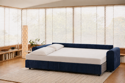Tria convertido en cama, con sábana bajera y dos almohadas, en un salón.